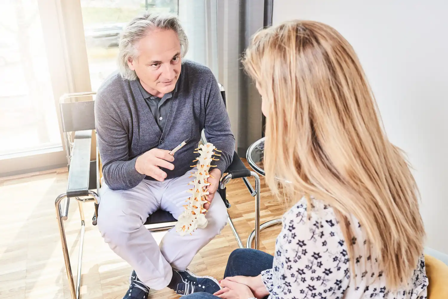 Ein Mann erklärt einer Frau anhand eines Wirbelsäulenmodells die Multimodale Schmerztherapie.
